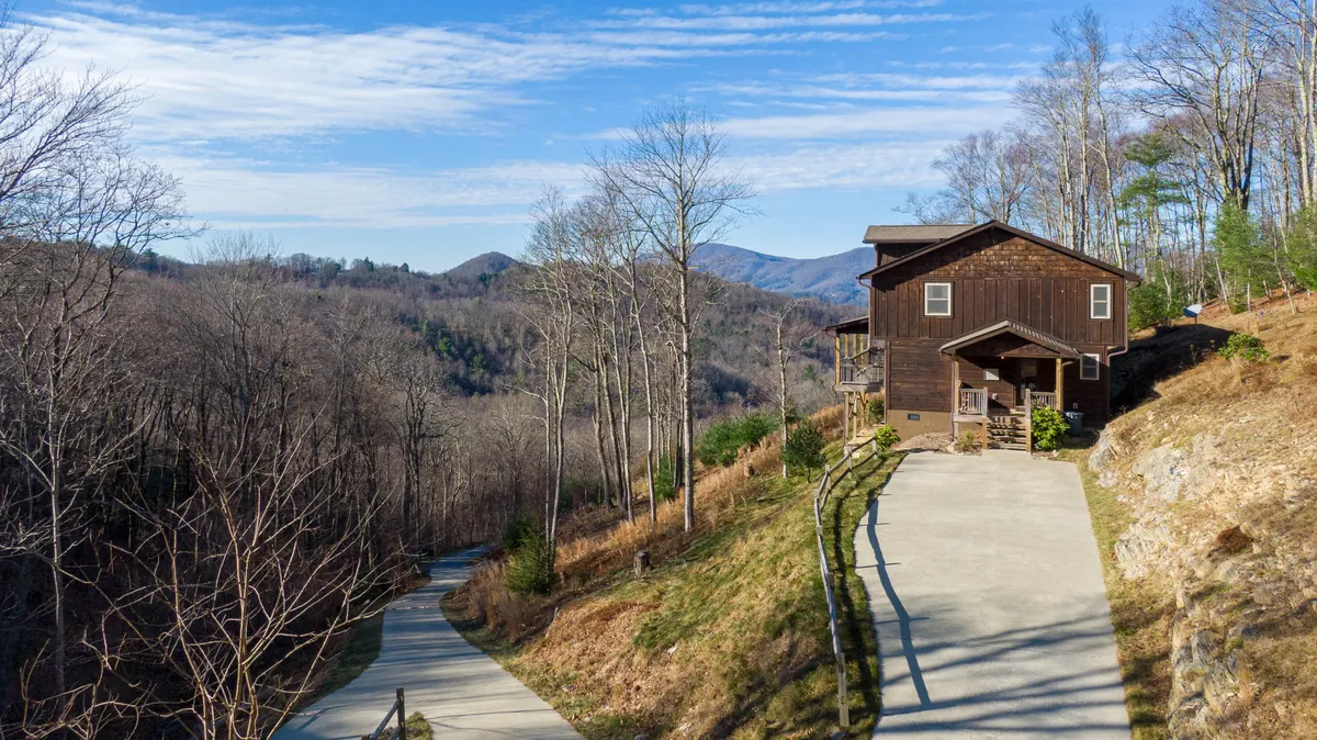 This image features the Skyland Cabin set amidst lush greenery, with the surrounding trees and expansive mountain views visible from the porch. The scene captures the essence of outdoor living, highlighting hiking and nature walks that start right from the doorstep, as well as the tranquil experience of relaxing on the porch while watching the sunrise or encountering wildlife.