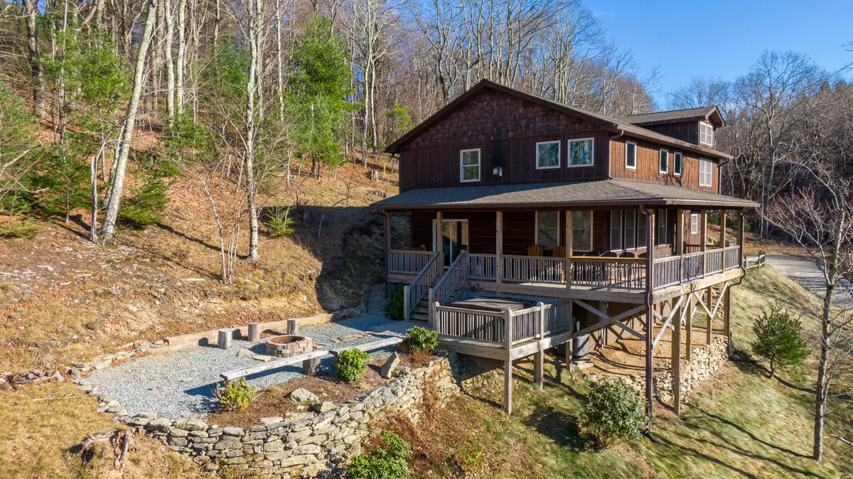 The hero image showcases a charming wooden cabin set amidst a beautifully landscaped garden. A spacious deck with inviting railings overlooks the mountains, while a cozy fire pit area promises warm evenings under the stars. The scene exudes comfort and relaxation, perfect for gatherings and enjoying nature.