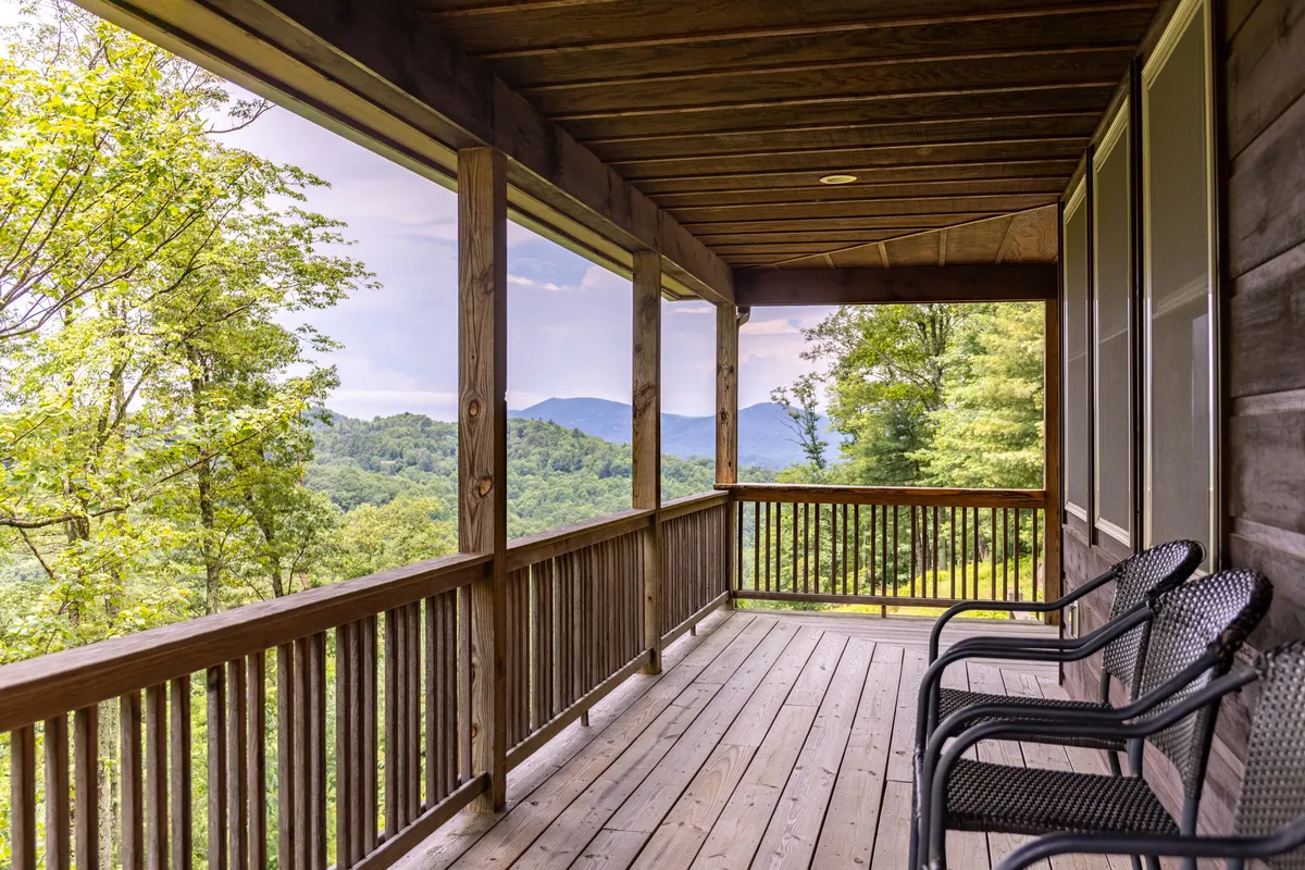 A serene view from the porch shows a wooden railing framing a sweeping mountain landscape, with seating ready for guests to relax and take in the sunrise or the night sky. The calm mood emphasizes the restorative side of mountain exploration.
