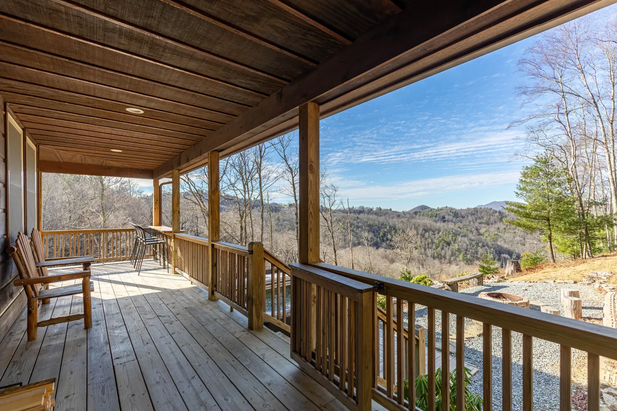 This image features a cozy porch with wooden railings and adjoining chairs, overlooking a stunning mountain view. The peaceful scene invites guests to relax, enjoy quiet moments together, and take in the beauty of sunrise or sunset.