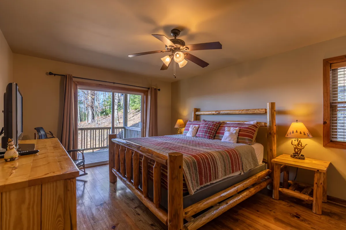 A bright, spacious bedroom with a plush bed and wooden furniture sits beside a large sliding glass door, which opens directly onto a private porch, letting in abundant natural light and offering views of the surrounding landscape. Soft linens and a cozy reading nook create an inviting, restful environment.