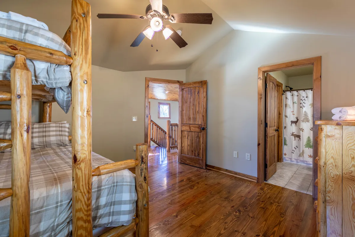 A cheerful, well-lit bunk room features queen-over-queen bunk beds with a trundle, warm wood finishes, and easy access to an ensuite bathroom. The space is inviting and flexible, ideal for families or groups.