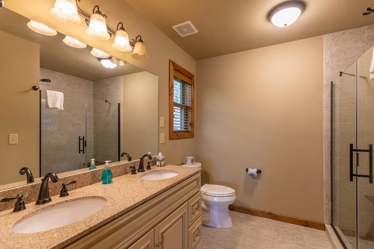 A bright, modern bathroom with a double vanity, a glass-enclosed shower, and ample natural light streaming in from a window. The elegant finishes and spa-inspired design create a soothing atmosphere for relaxation and rejuvenation.